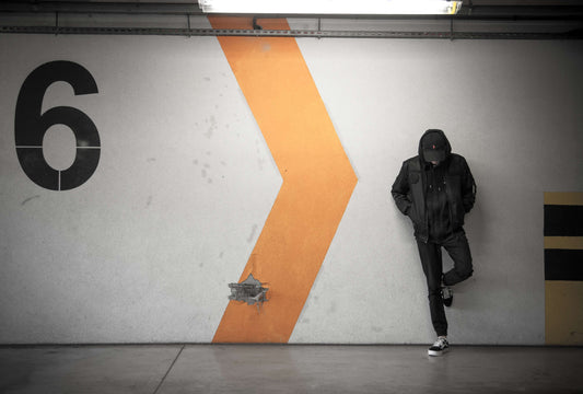 Man dressed in streetwear resting against a wall.