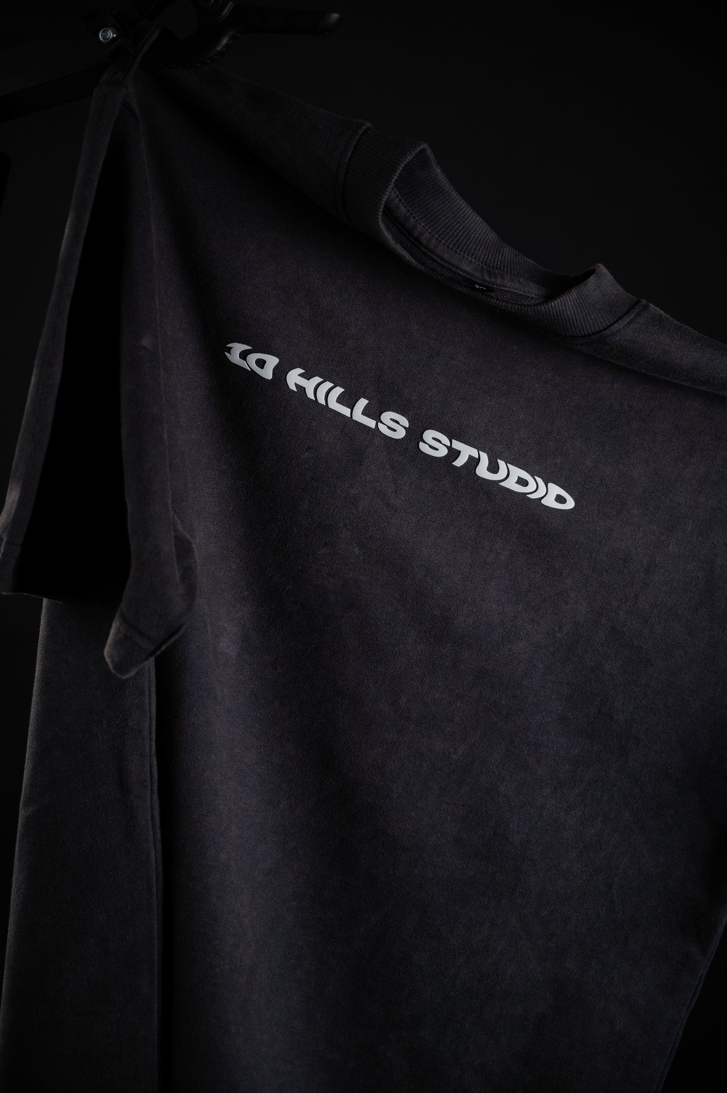Front view of 10 Hills Studio Vintage Black Logo Tee hanging in a dark contrast style photography
