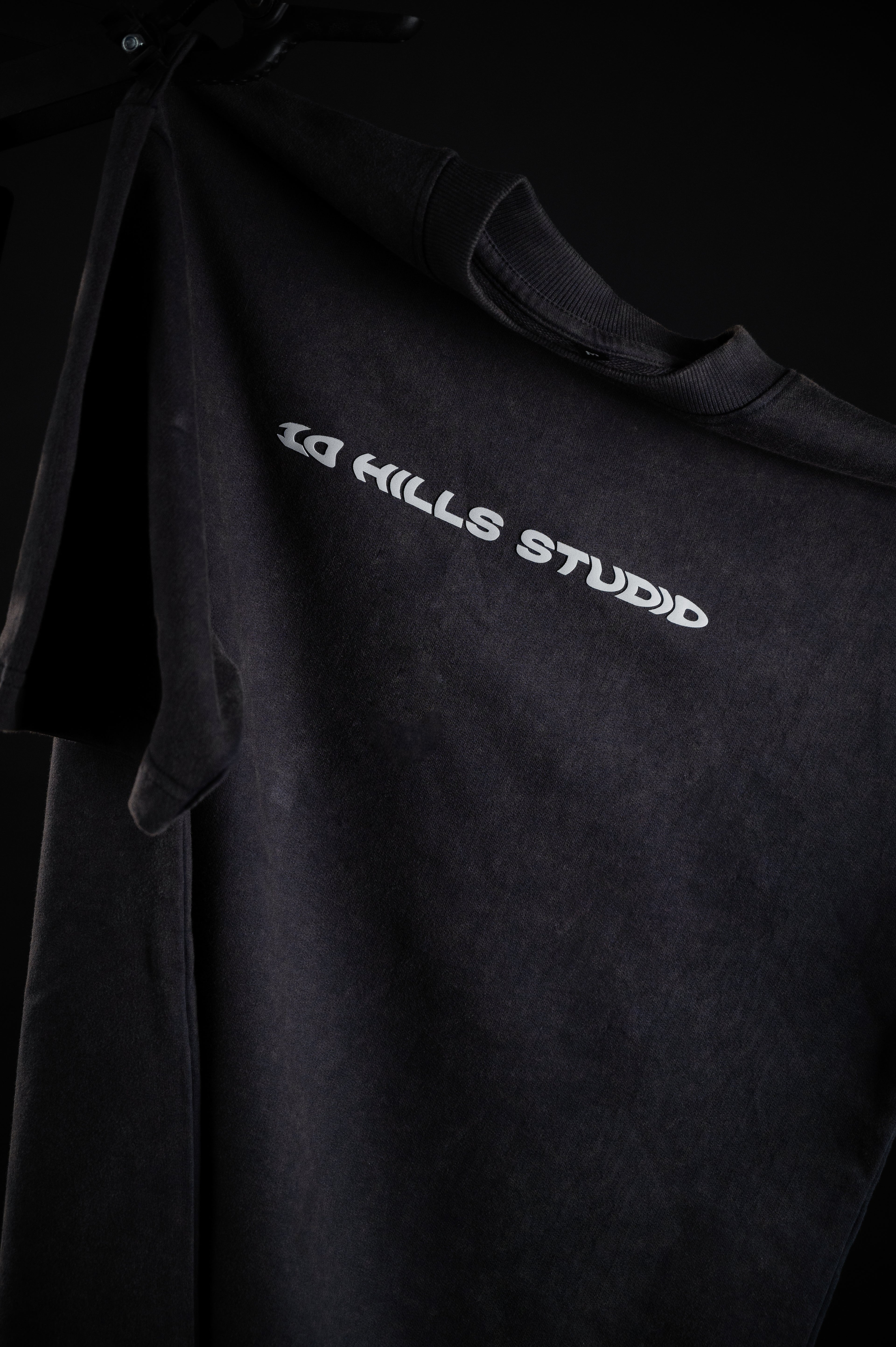 Front view of 10 Hills Studio Vintage Black Logo Tee hanging in a dark contrast style photography