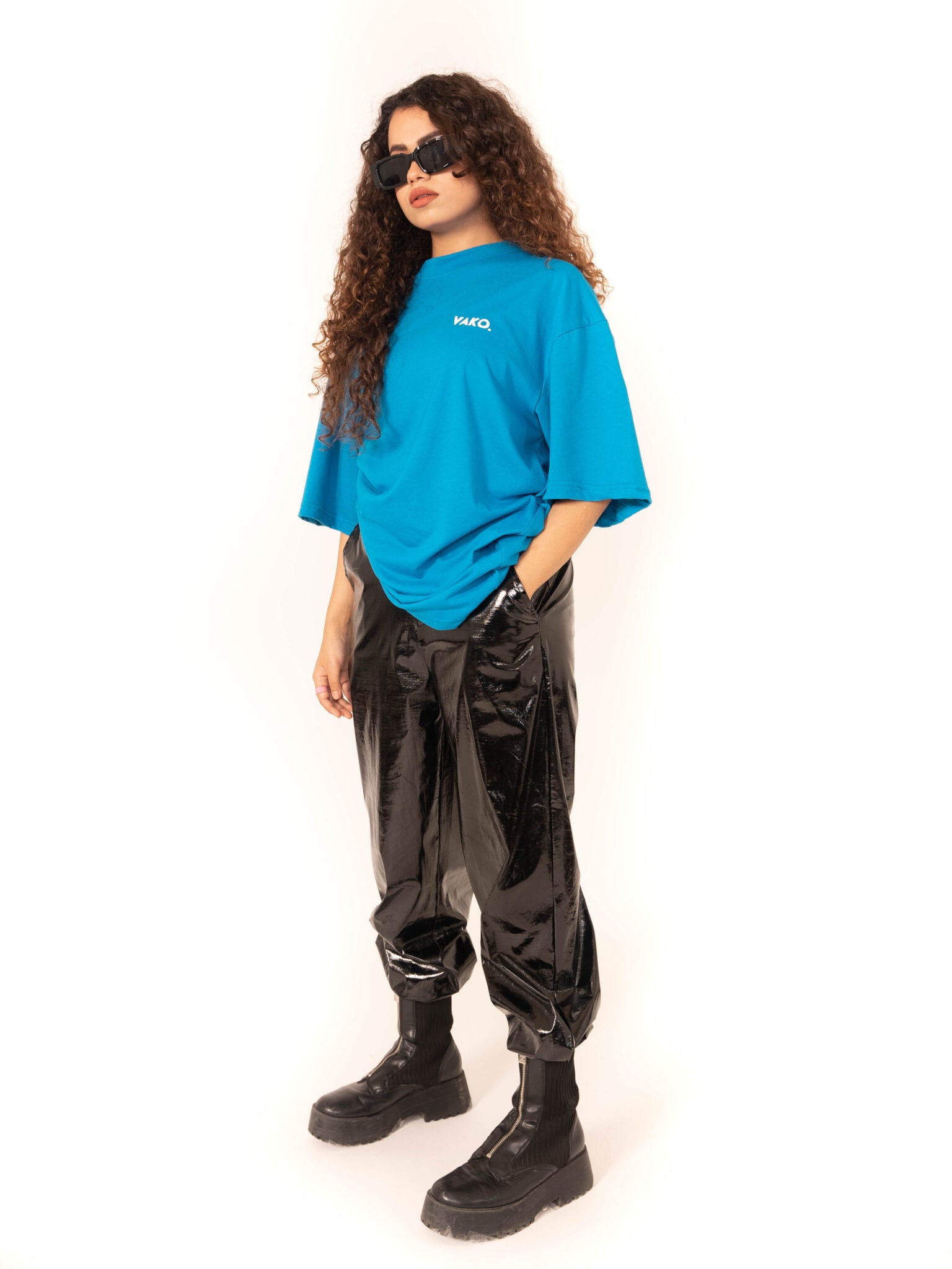 Female Model showcasing front of Vako Blue T-Shirt with glossy black pants and chunky boots, accessorized with oversized sunglasses
