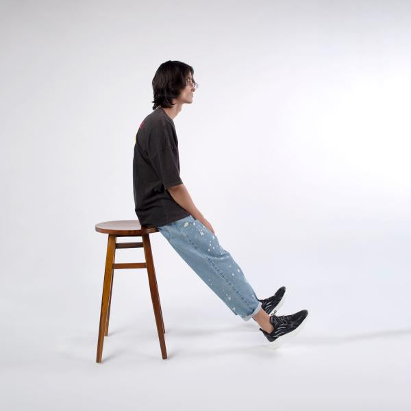 Side of view of male model wearing A Skating Monk Black 'Reborn' Oversize Tee while sitting on a chair